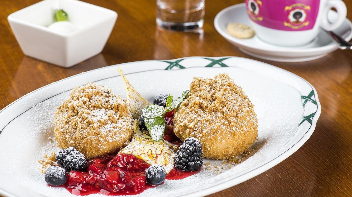 Ein Dessertteller mit knusprigen Süßspeisen, garniert mit Beeren und einer fruchtigen Sauce. Im Hintergrund steht eine Tasse Kaffee und ein kleines Schälchen. | © Tauroa GmbH