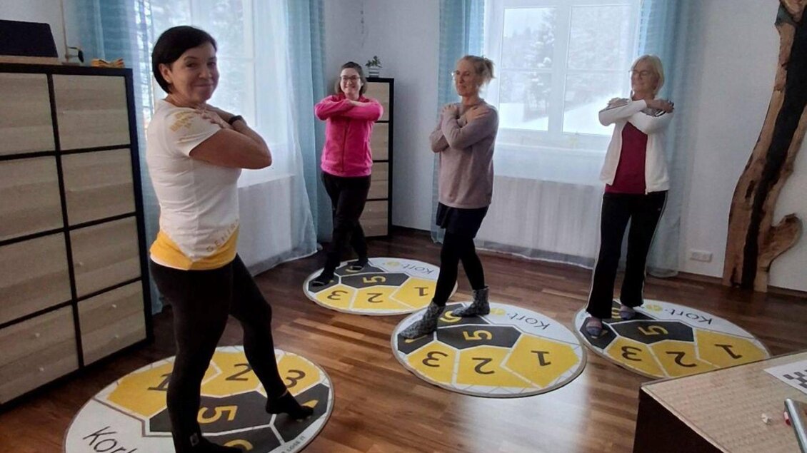 Vier Frauen stehen auf farbigen Bodenmatten in einem Raum. Sie üben gemeinsam eine Fitnessübung. | © Sabines Glücksplatz_Holzer