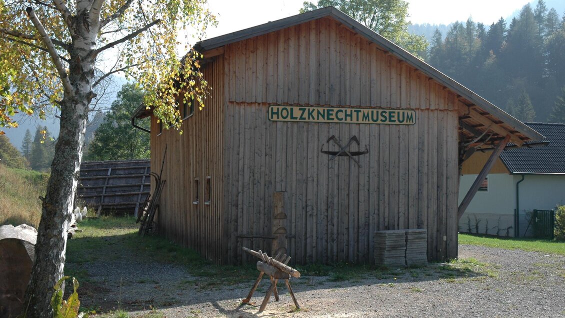 Ein gemütliches Holzhaus mit der Beschriftung "Holzknechtmuseum". Es steht in einer ruhigen Umgebung mit Bäumen und sanften Hügeln. | © Holzknechtmuseum