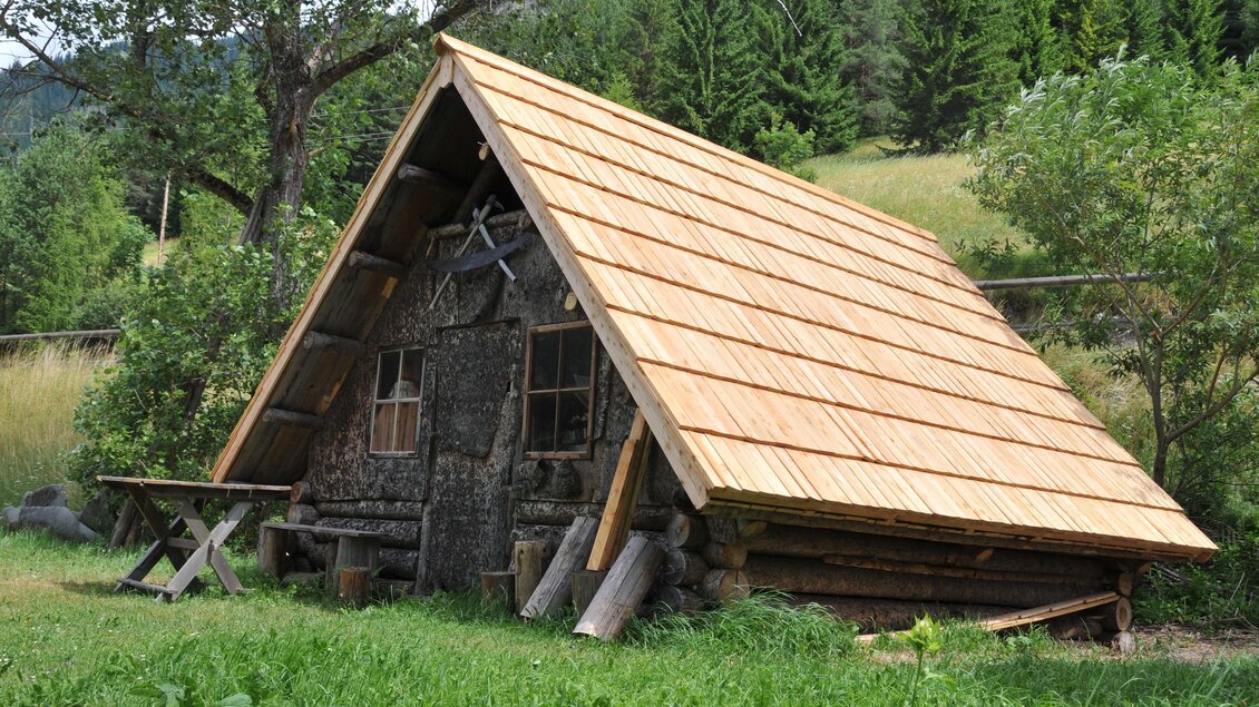 Ein kleines, rustikales Holzhaus mit einem schrägen Dach steht in der Natur. Umgeben von Bäumen und Wiese strahlt es Gemütlichkeit und Einfachheit aus. | © Holzknechtmuseum
