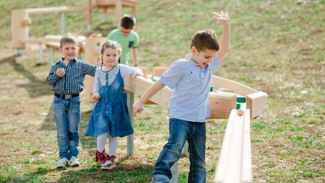 Eine Gruppe von Kindern spielt im Freien auf einem Spielplatz. Sie interagieren mit Holzelementen und haben Spaß miteinander. | © Karin Bergmann