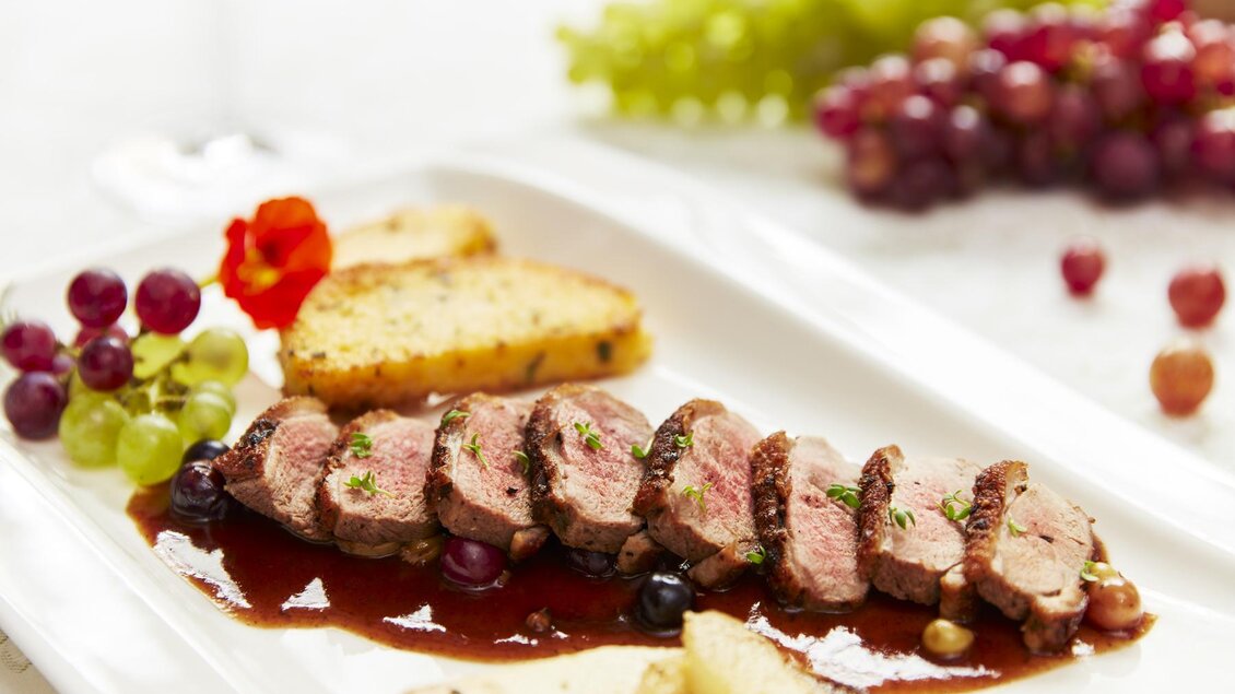 Ein appetitliches Gericht mit dünn geschnittenem Fleisch, garniert mit einer Sauce. Dazu gibt es knusprige Brötchen und frische Trauben. | © Domittner