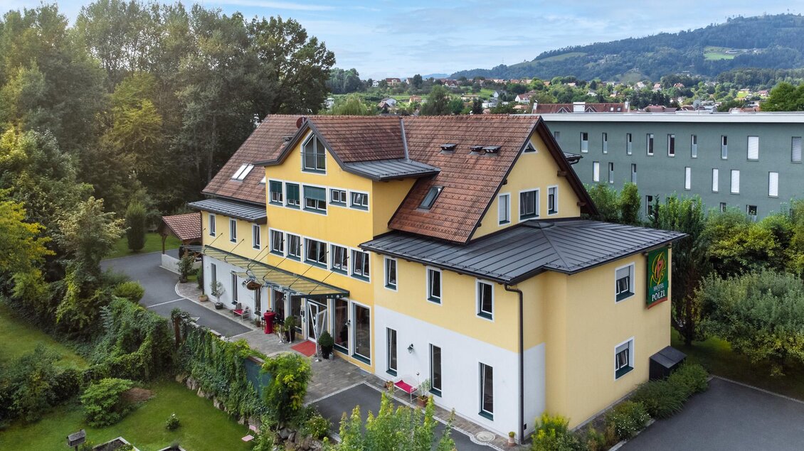 Ein großes, gelbes Gebäude mit mehreren Fenstern und einem roten Dach. Umgeben von einem gepflegten Garten und Bäumen.