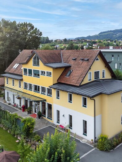 Ein großes, gelbes Gebäude mit mehreren Fenstern und einem roten Dach. Umgeben von einem gepflegten Garten und Bäumen.