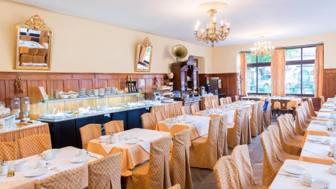 Ein elegantes Restaurant mit Tischen, die mit orangefarbenen Tischdecken gedeckt sind. Der Raum ist hell erleuchtet und verfügt über große Fenster und stilvolle Dekorationen. | © CORDES-Werbeconsulting GmbH