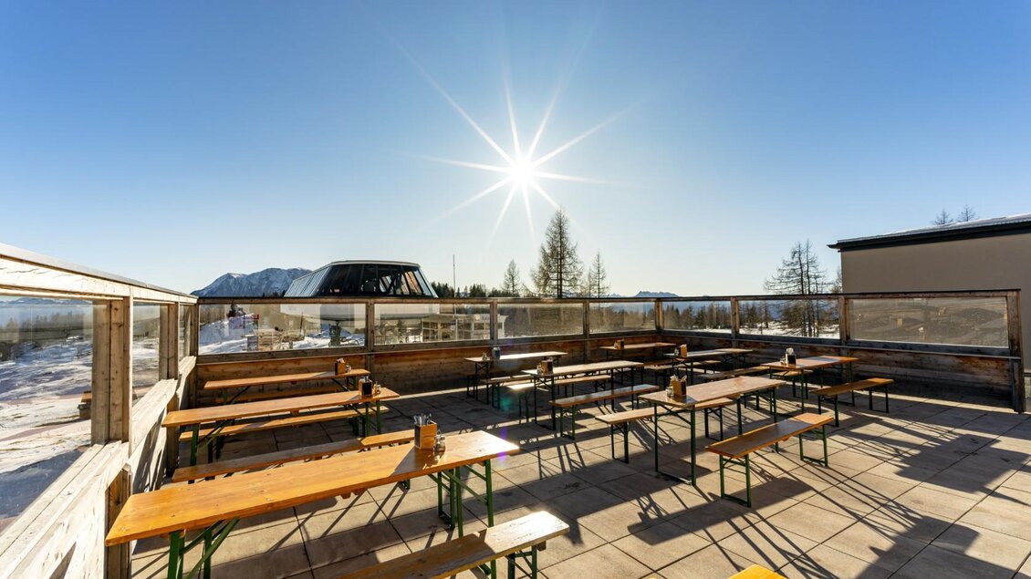 Eine sonnige Terrasse mit Holzbank und Tischen in den Bergen. Der klare Himmel und die strahlende Sonne schaffen eine einladende Atmosphäre. | © Die Tauplitz, Thomas Hofer