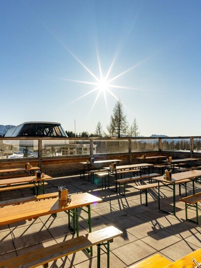 Eine sonnige Terrasse mit Holzbank und Tischen in den Bergen. Der klare Himmel und die strahlende Sonne schaffen eine einladende Atmosphäre. | © Die Tauplitz, Thomas Hofer