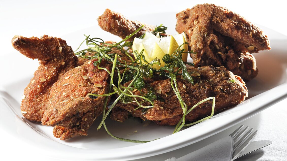 Ein Teller mit knusprig gebratenem Hühnchen, garniert mit frischen Kräutern und Zitronenscheiben. Das Gericht ist appetitlich angerichtet. | © Bernhard Bergmann