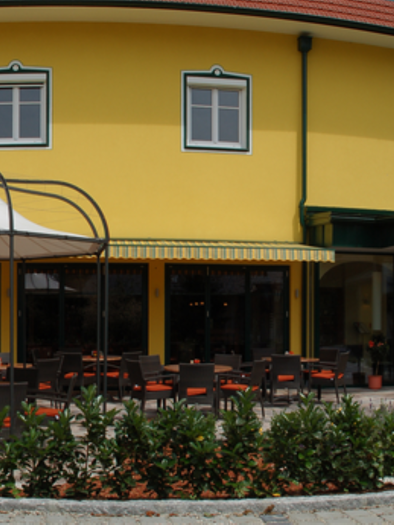 Ein gemütliches Restaurant mit einer gelben Fassade und einer einladenden Terrasse. Rund um die Terrasse sind grüne Pflanzen angeordnet. | © Hotel-Restaurant Neuhold