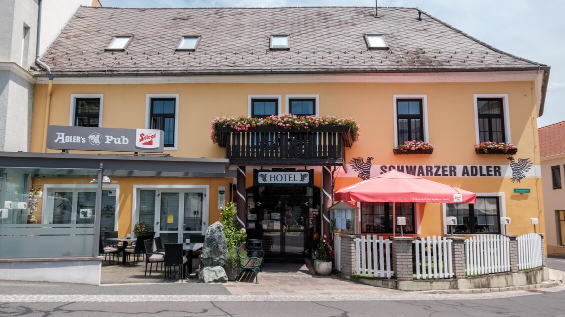 Ein gelbes Gebäude mit einem Restaurant und einer Bar. Vor dem Haus gibt es Sitzmöglichkeiten im Freien und Blumen in den Fenstern. | © Hotel Schwarzer Adler