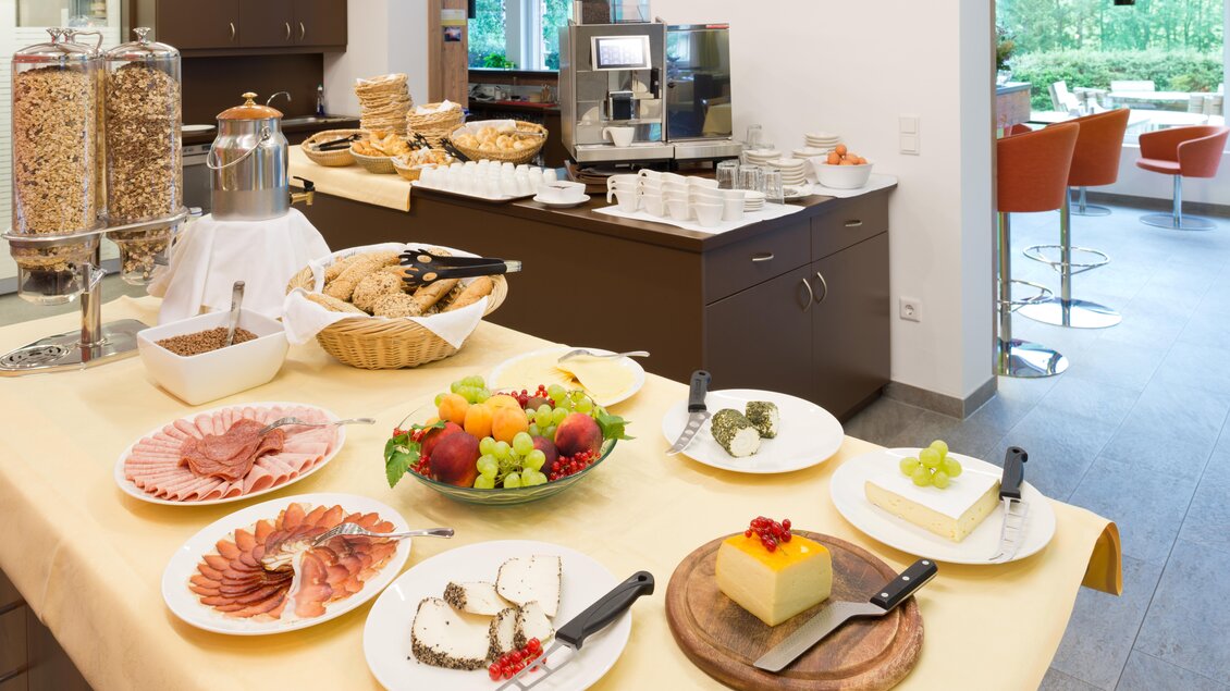 Ein liebevoll gedeckter Tisch mit einer Auswahl an Wurst, Käse, frischem Obst und Gebäck. Im Hintergrund sieht man eine Kaffeemaschine und eine gemütliche Sitzgelegenheit. | © Hotel Seebacherhof_(c)Hagspiel