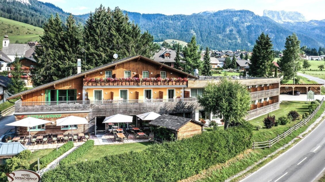 Ein charmantes Hotel in malerischer Umgebung mit einer ruhigen Straße und grünen Wiesen. Die Terrasse bietet Platz zum Entspannen und Genießen der Natur. | © Hotel Seebacherhof, Andreas Maxones, Andrea Koch