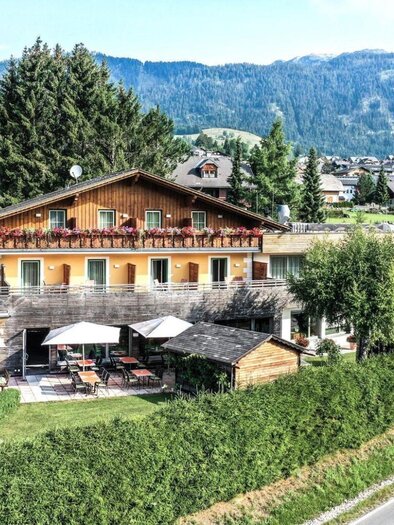 Ein charmantes Hotel in malerischer Umgebung mit einer ruhigen Straße und grünen Wiesen. Die Terrasse bietet Platz zum Entspannen und Genießen der Natur. | © Hotel Seebacherhof, Andreas Maxones, Andrea Koch