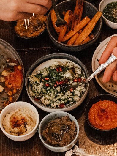 A laid table with various delicious dishes and sides. Hands reaching for the food create a convivial atmosphere. | © Hummel Graz