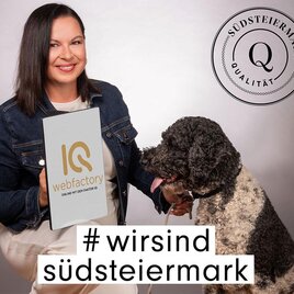 Eine Frau hält ein Schild mit der Aufschrift „IQ webfactory“ und sitzt neben einem Hund. Im Hintergrund ist das Logo „Südsteiermark Qualität“ sichtbar. | © (C) Qualtität Südststeiermark