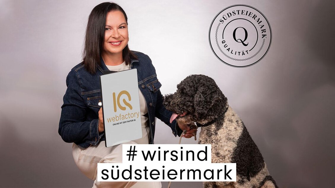 Eine Frau hält ein Schild mit der Aufschrift „IQ webfactory“ und sitzt neben einem Hund. Im Hintergrund ist das Logo „Südsteiermark Qualität“ sichtbar. | © (C) Qualtität Südststeiermark