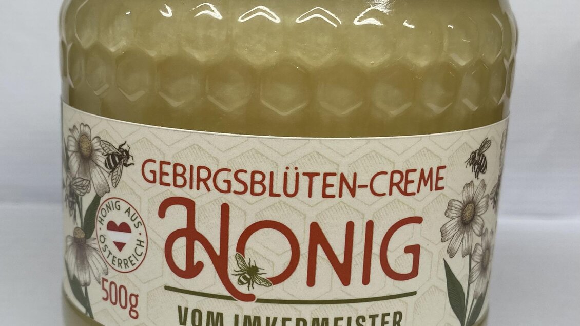 Ein Glas Gebirgsblüten-Cremehonig mit dem Etikett "Honig vom Imkermeister." Die Verpackung ist rund und hat einen goldenen Deckel. | © Gebirgsimkerei Schladming Johann Lettner