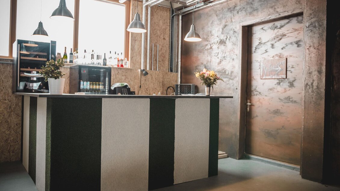 Ein moderner Empfangsbereich mit einem stilvollen Tresen und einer dekorativen Wand. Helle Fenster lassen viel Licht herein und schaffen eine einladende Atmosphäre. | © Indoor Golf Studio