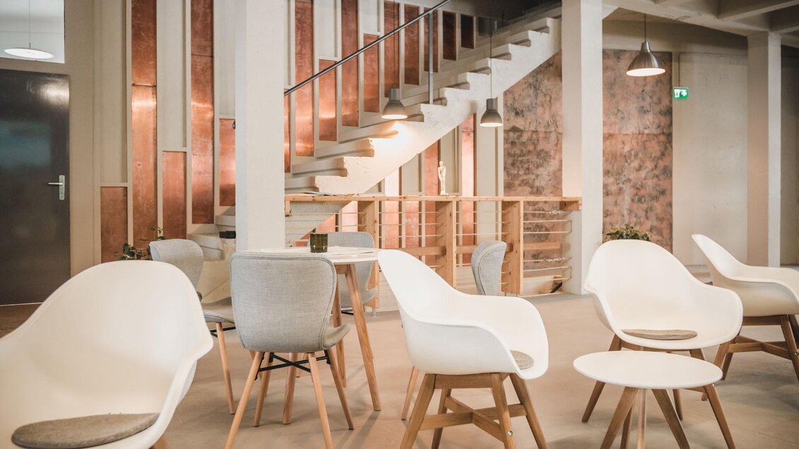 Ein modernes Innenraum mit eleganten Stühlen und einem runden Tisch. Im Hintergrund sind eine Treppe und gepflegte Wände zu sehen. | © Indoor Golf Studio