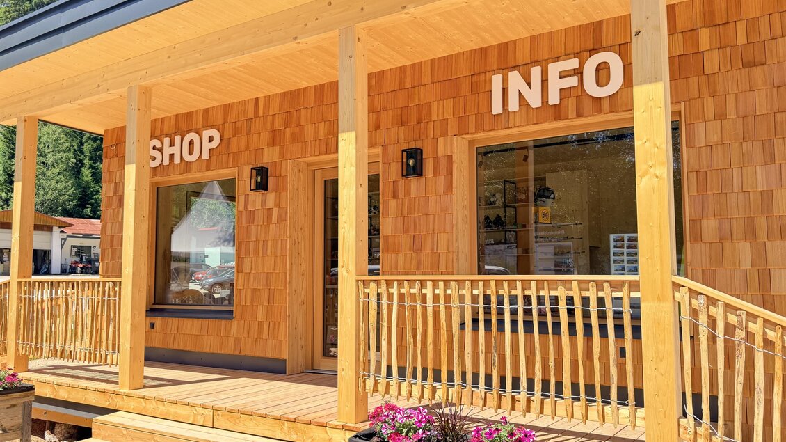 Ein Hölzernes Gebäude mit den Schildern "SHOP" und "INFO" an der Fassade. Der Eingang ist mit einer kleinen Veranda und Blumenkästen geschmückt. | © Rittisberg