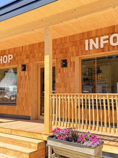 Ein Hölzernes Gebäude mit den Schildern "SHOP" und "INFO" an der Fassade. Der Eingang ist mit einer kleinen Veranda und Blumenkästen geschmückt. | © Rittisberg
