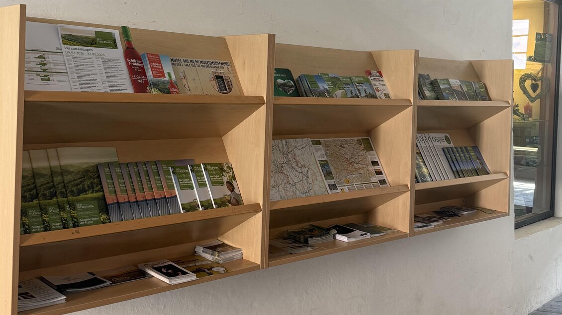 Ein offenes Regal mit mehreren Fächern, gefüllt mit Broschüren und Informationsmaterialien. Die Wand ist hell und die Regale aus Holz. | © TVB Südsteiermark