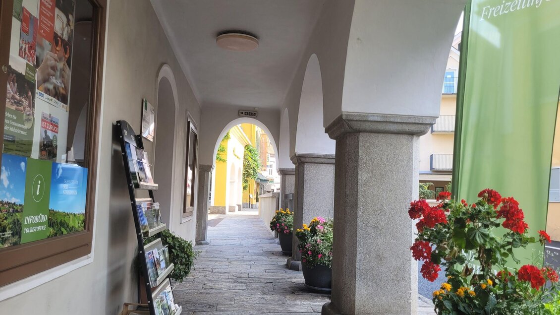 Ein schmaler Durchgang mit Steinboden und hohen Bögen. An den Wänden stehen Zeitungsständer und blühende Pflanzen sorgen für Farbe. | © TV Südsteiermark - Irene Löschnig