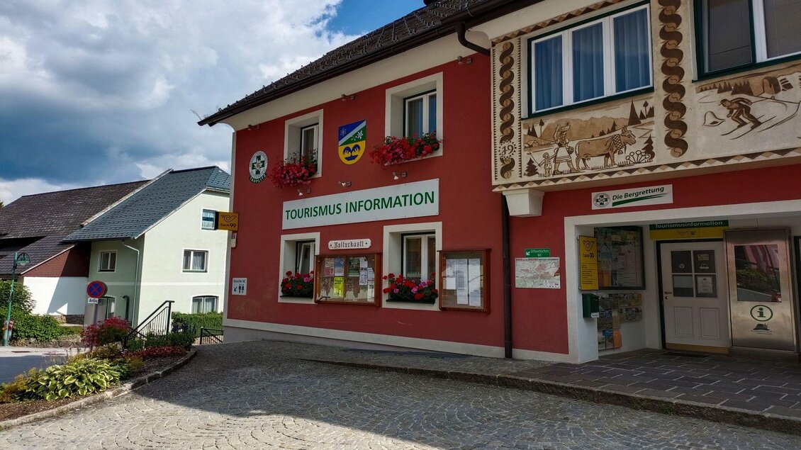 Ein farbenfrohes Gebäude mit der Aufschrift „TOURISMUS INFORMATION“. Der Eingang ist gut sichtbar und umgeben von Blumen. | © TVB Ausseerland Salzkammergut/Kolb