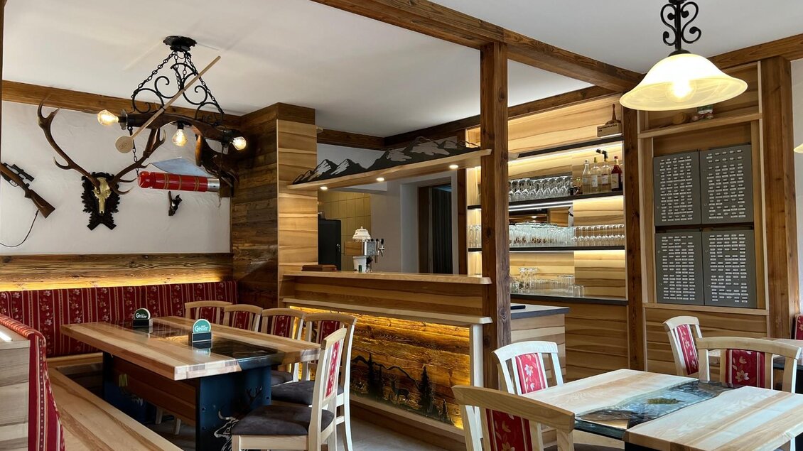 Ein gemütliches Restaurant mit Holzinterieur und traditioneller Dekoration. Tische mit roten Stoffen und eine freundliche Atmosphäre laden zum Essen ein. | © Corina Präsoll