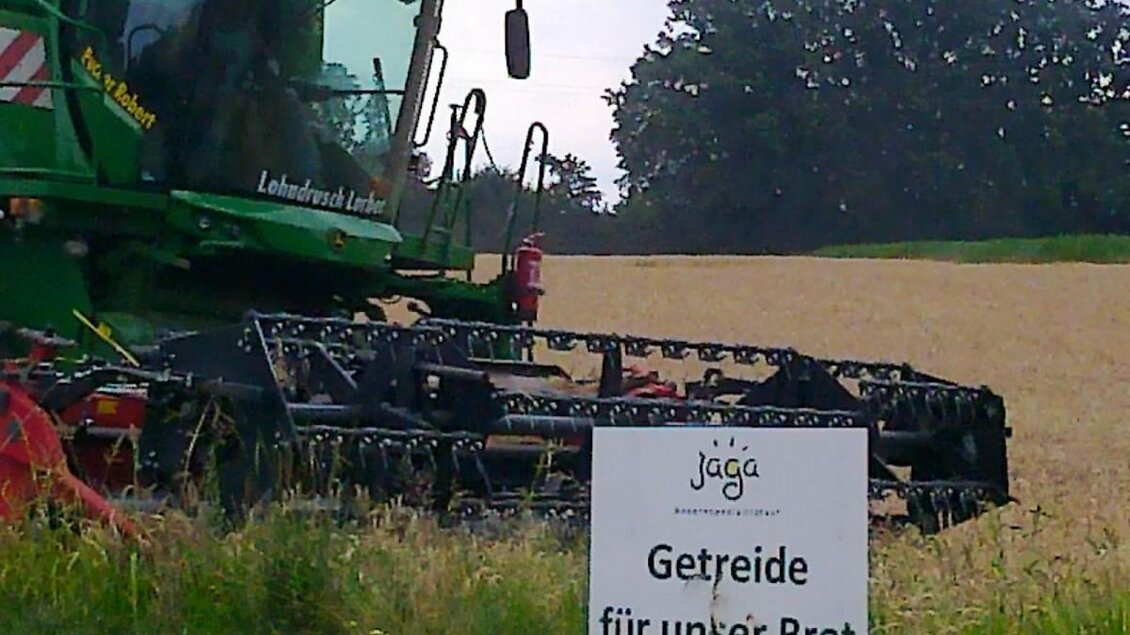 Ein landwirtschaftlicher Mähdrescher steht auf einem Feld. Daneben steht ein Schild mit der Aufschrift „Getreide für unser Brot“. | © LK Stmk