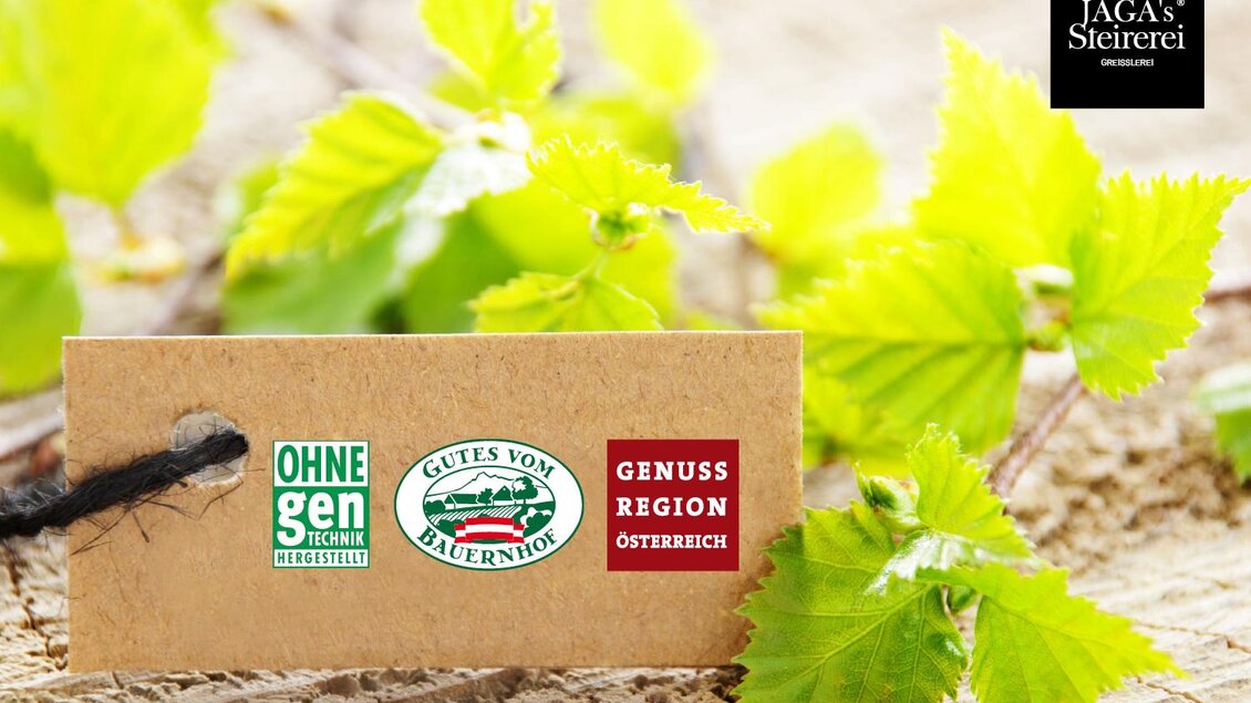 Ein braunes Etikett mit verschiedenen Logos und Labels liegt auf einem Holzuntergrund. Im Hintergrund sind frische grüne Blätter zu sehen. | © LK Stmk