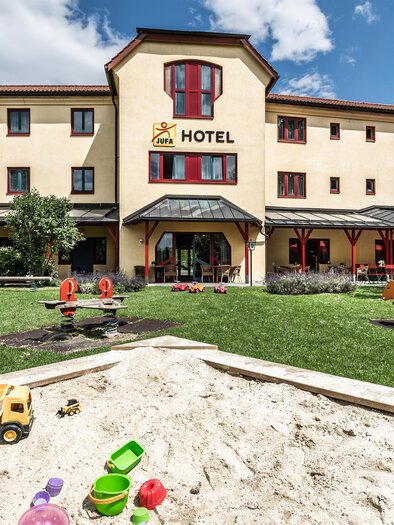 JUFA Hotel in Maria Lankowitz mit Terrasse, Garten und Spielplatz mit Sandkiste vor dem Gebäude. | © Lipizzanerheimat-Lenz