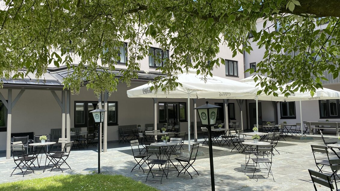 Außenterrasse im JUFA Hotel Maria Lankowitz mit Sitzplätzen, Sonnenschirmen und Grünfläche vor dem Gebäude. | © Lipizzanerheimat-IQ Foto