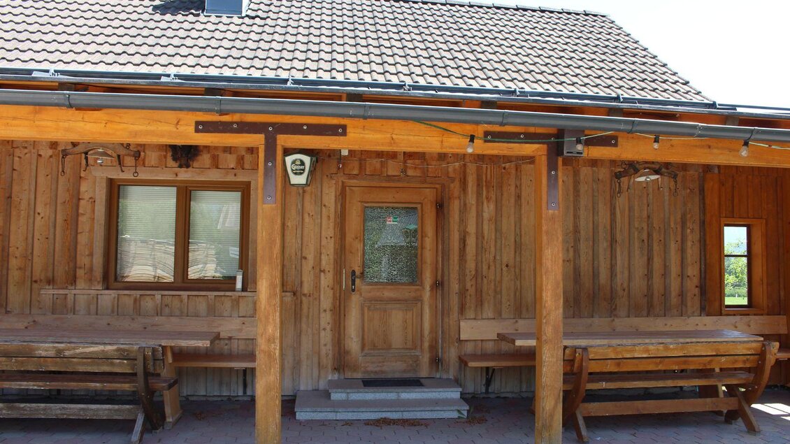 Ein traditionelles Holzhaus mit einem massiven Dach. Vor dem Haus befinden sich Holzbänke und Tische. | © Jan`s Jausenhütt`n