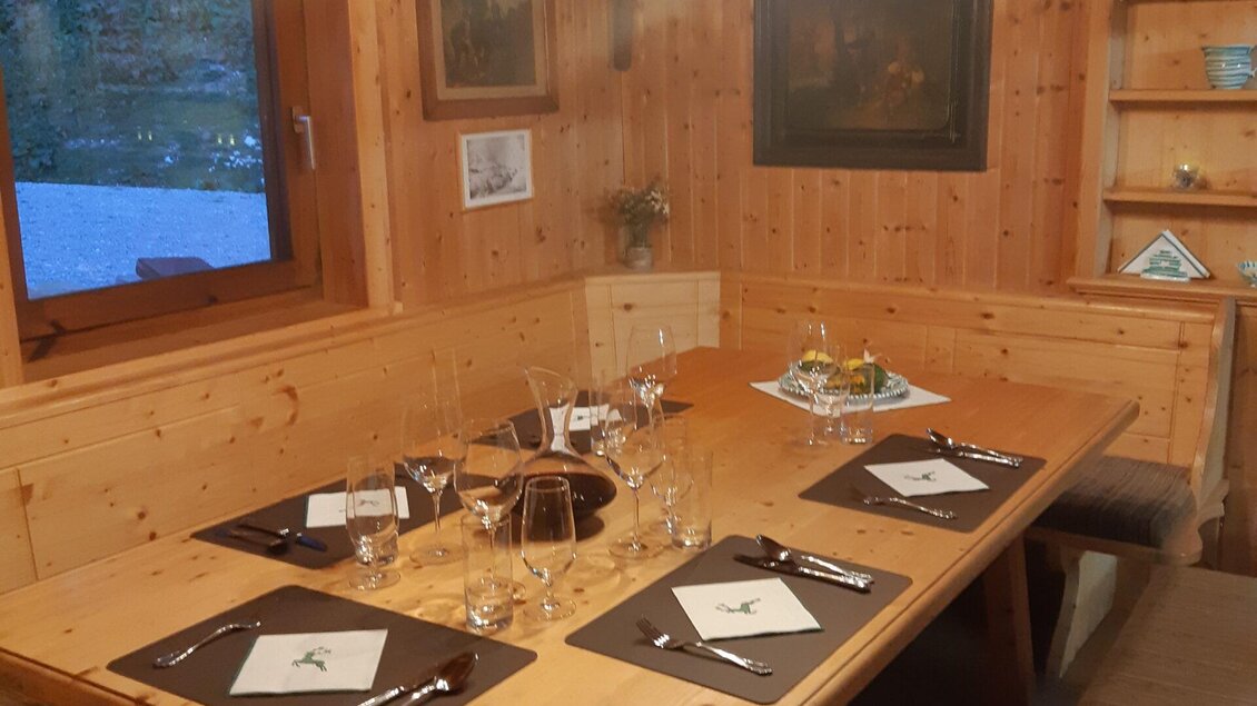 Ein rustikales Esszimmer mit einem großen Holztisch und eleganten Gläsern. Die Wände sind mit Jagdtrophäen dekoriert und ein warmes Licht sorgt für eine gemütliche Atmosphäre. | © TV Erzberg Leoben