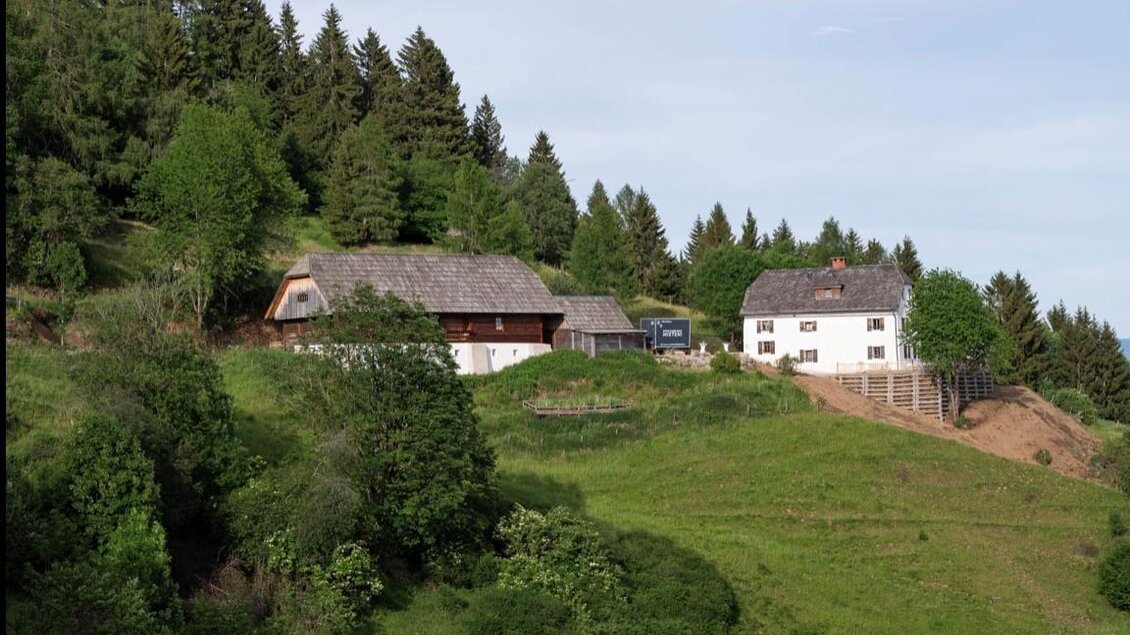 Eine idyllische Landschaft mit grünen Hügeln und Wald. Im Vordergrund sind zwei charmante Häuser zu sehen. | © Jausenstation Höhn