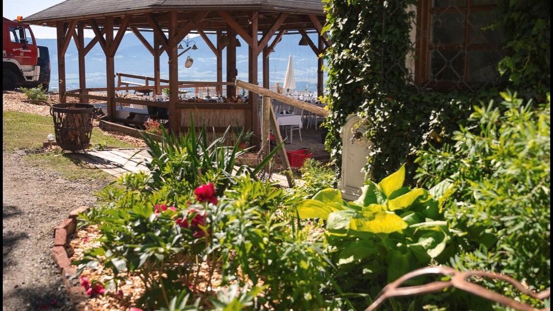 Ein schöner Pavillon umgeben von bunten Blumen und grünem Laub. Im Hintergrund ist das Wasser zu sehen. | © Jausenstation Höhn