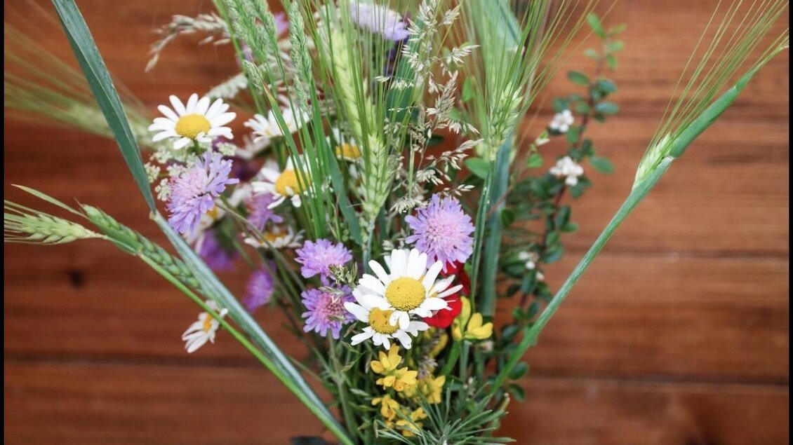 Ein schöner Blumenstrauß mit verschiedenen Wildblumen und Gräsern in einer Glasvase. Die Farben sind lebhaft und harmonisch. | © Jausenstation Höhn