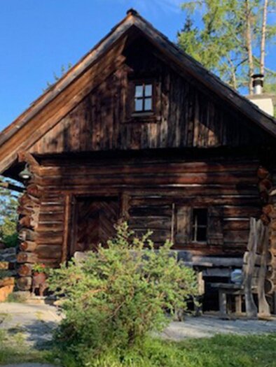 Eine rustikale Holzhütte umgeben von Bäumen und Grün. Der Himmel ist blau und die Atmosphäre ist friedlich. | © Schererwirt