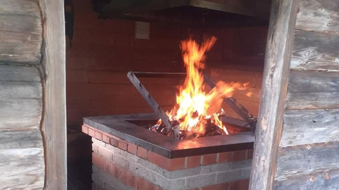 Ein offener Kamin in einer rustikalen Hütte. Flammen lodern aus dem Feuer, das für gemütliche Wärme sorgt.