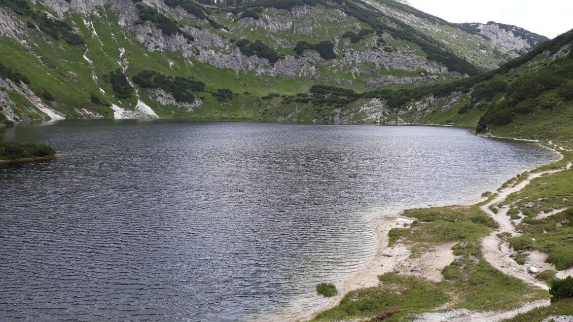 Ein ruhiger Bergsee umgeben von grünen Wiesen und steilen Hängen. Die Landschaft ist beeindruckend und lädt zur Erholung ein. | © Stephanie Bor