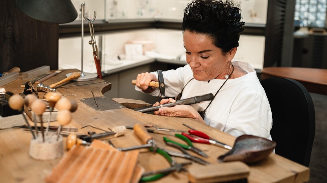Frau Gressl bearbeitet ein Schmuckstück mit Hammer und Werkzeug an der Werkbank von Juwelier Gressl. | © Bernd Grosseck
