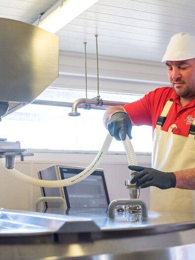 A man is working in a food processing facility. He operates a machine with hoses and focuses on production. | © RM SWS GmbH | webquartier.at