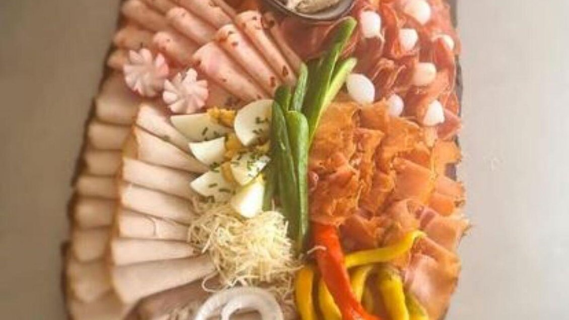 Eine große Wurst- und Käseplatte, kunstvoll auf einem Holzbrett angerichtet. Sie zeigt verschiedene Fleischsorten, Gemüse und garnierte Elemente. | © Köll Fleischfachgeschäft &amp; Catering