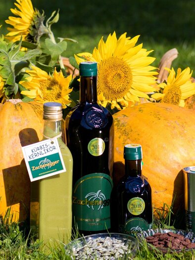 A collection of pumpkins and sunflowers in nature. Next to them are bottles of oil and other products that represent the harvest. | © Region Graz -  Harry Schiffer