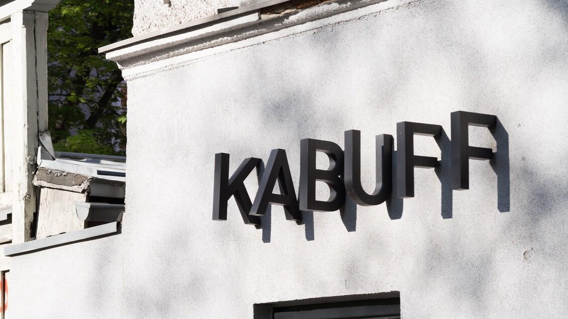 Ein modernes Gebäude mit einer hellen Fassade. Der Schriftzug "KABUFF" ist deutlich sichtbar und wirft einen Schatten auf die Wand. | © Kabuff