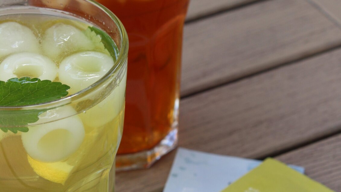 Zwei erfrischende Getränke auf einem Tisch. Ein Glas enthält einen gelben Drink mit Limonenscheiben und Minze, das andere ist ein dunkler Tee mit Eis. | © Katharina Zeiler