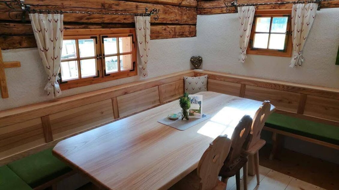 Ein gemütlicher Essbereich aus Holz mit einem großen Tisch und Bänken. Große Fenster lassen viel Licht herein und schaffen eine einladende Atmosphäre. | © Kainrath