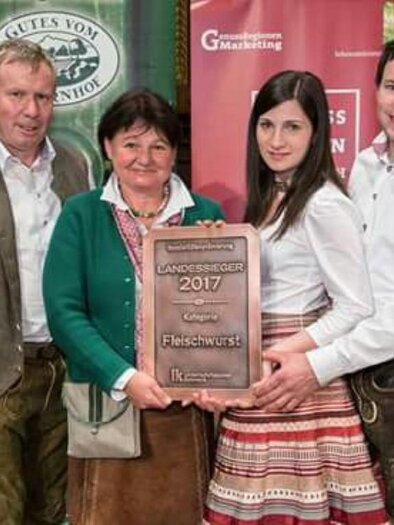 A group of four people stands together and holds an award for the best sausage. They are wearing traditional costumes and smiling at the camera. | © Fam. Posch