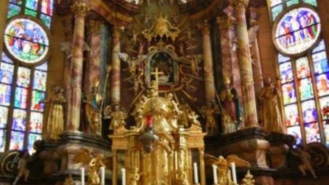 Ein prachtvoller Altar mit goldenen Verzierungen und bunten Fensterrosetten. Der Raum ist hell erleuchtet und strahlt eine spirituelle Atmosphäre aus.